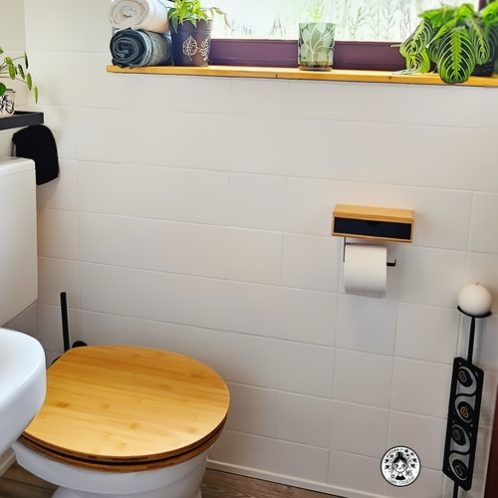 Aseo pequeño reformado con tapa de inodoro de bambú, decoración natural y azulejos blancos pintados.