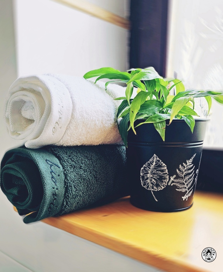 Toallas enrolladas y planta decorativa sobre repisa de madera en un aseo reformado.