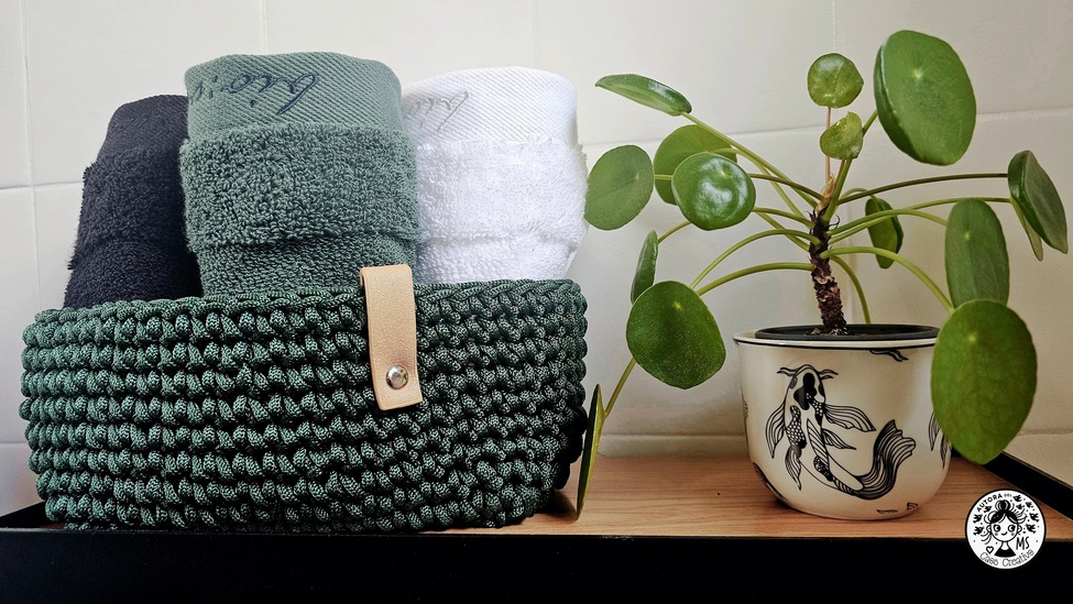 Cesta decorativa con toallas enrolladas y planta Pilea en maceta ilustrada en baño renovado.