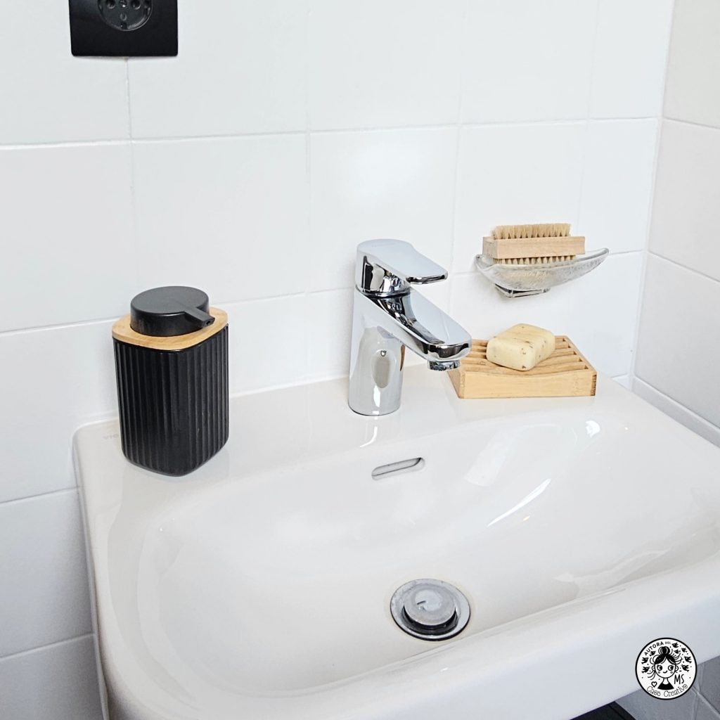 Lavabo renovado en aseo pequeño con detalles en negro y madera