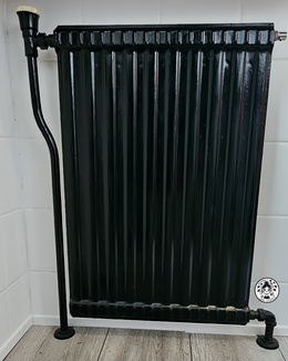 Radiador antiguo restaurado con pintura negra mate tras renovación del aseo.