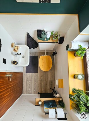 Vista superior del baño reformado con pintura blanca, toques en negro y madera, y decoración con plantas.