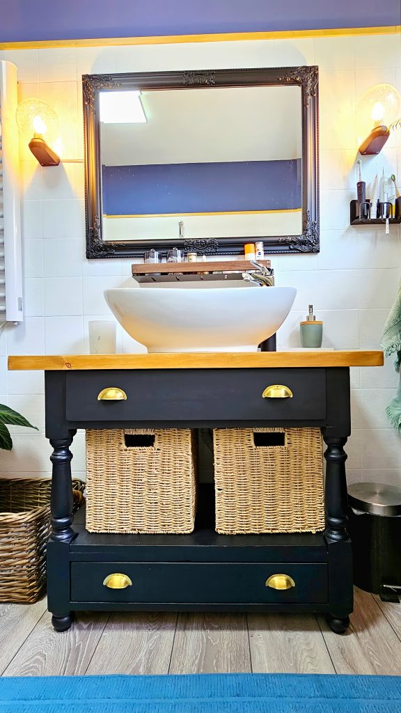 Mueble de lavabo negro con encimera de madera y lavabo sobre encimera, acompañado de espejo negro y apliques de luz en la reforma del baño