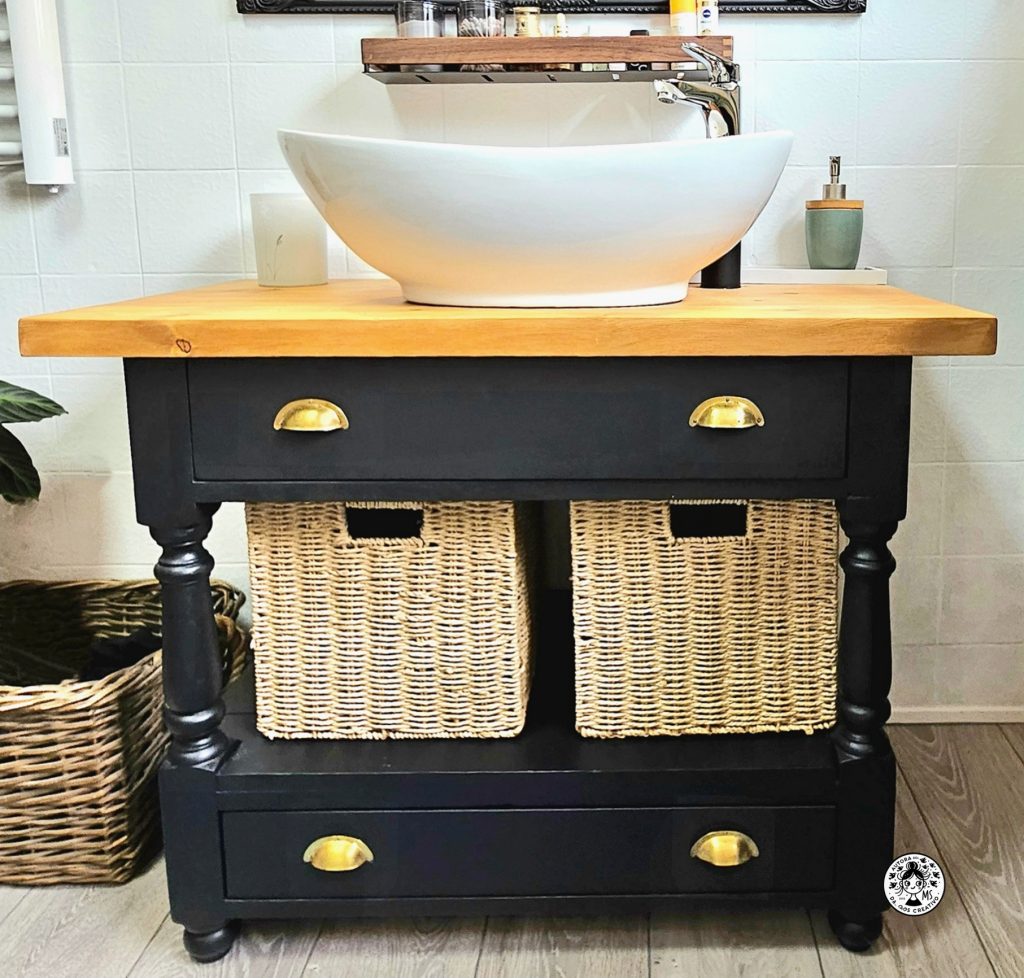Mueble de lavabo renovado en negro mate con tapa de madera natural y cestas de mimbre, resultado final de la reforma del baño