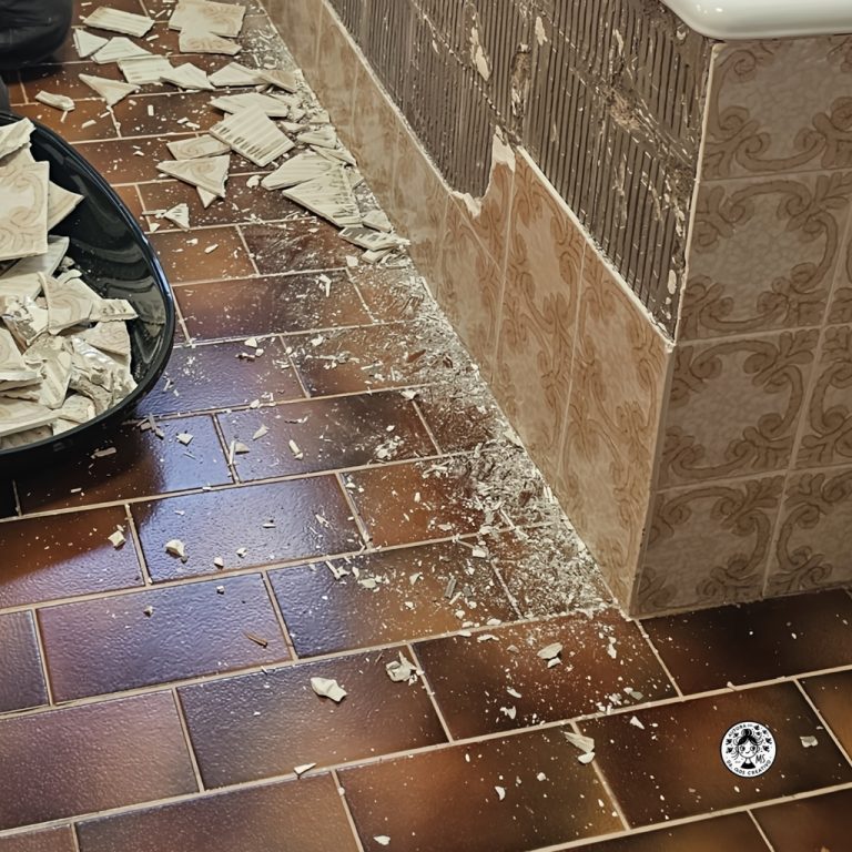 Proceso de quitar azulejos viejos del baño durante la reforma, escombros en el suelo.